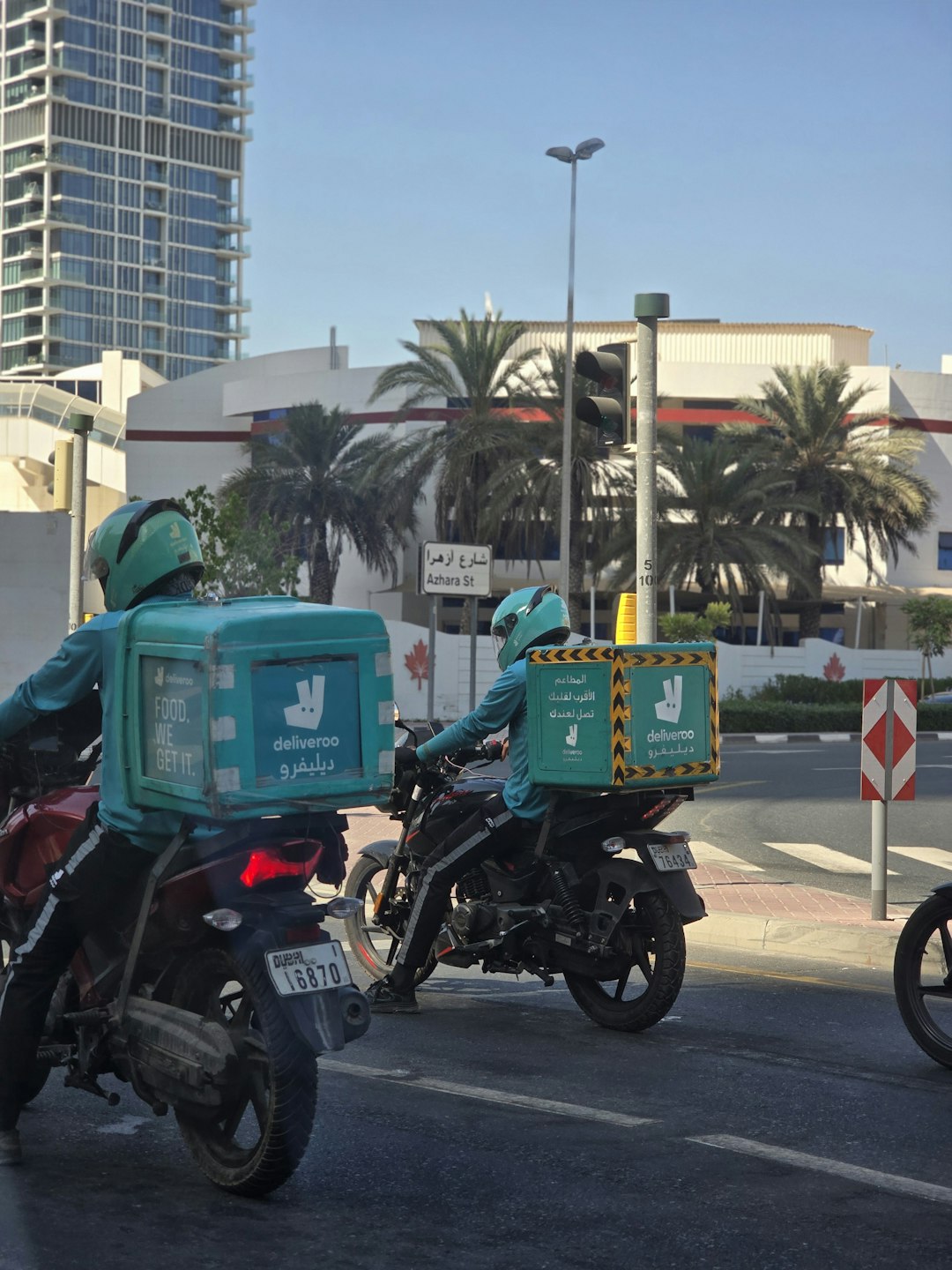 Deliveroo riders waiting at a traffic signal in Dubai, showcasing urban delivery services in action.