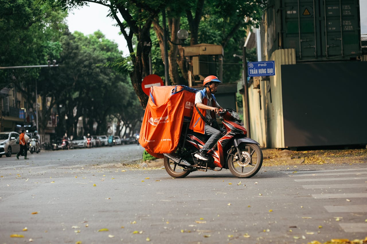 A delivery driver transports goods on a motorcycle in a bustling city street scene.